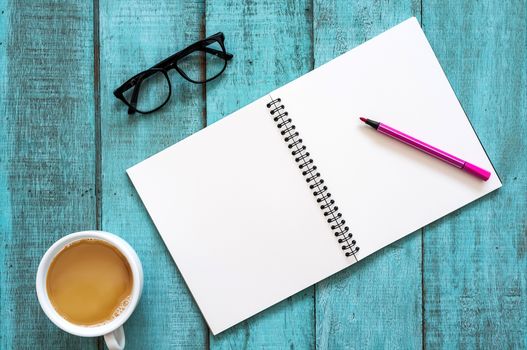 Blue wooden desk table with notebook, color pen, eyeglasses and cup of coffee. Top view with copy space, flat lay.