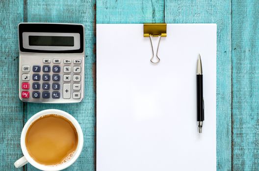 Blue wooden desk table with paper ream, pen, calculator and cup of coffee. Top view with copy space, flat lay.