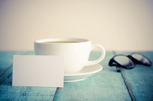 Blank business cards, cup of coffee and eyeglasses on blue wooden table. Vintage filter.