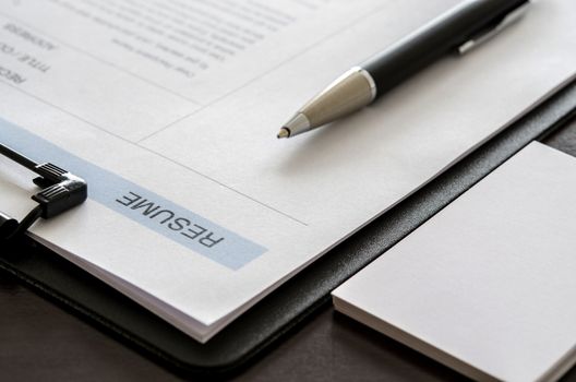 Close-up resume form, pen and business card on wooden desk.