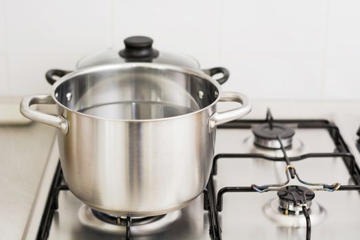 Close-up of stainless steel cooking pot on gas stove in contemporary upscale modern home kitchen. Selective focus on pot.