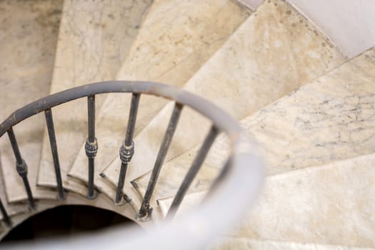 Upside view of indoor spiral winding staircase with black metal ornamental handrail.