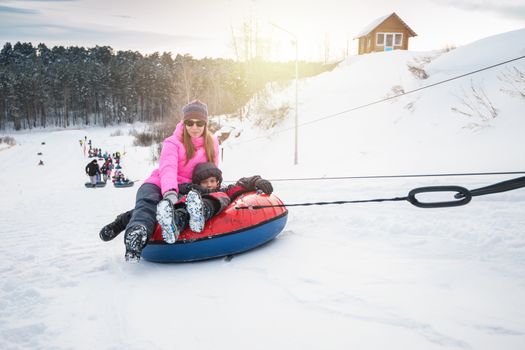 Mother and her son having fun on a snow tube, at beauty winter day