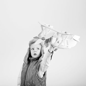 Child boy playing with paper toy airplane and dreaming of becoming a pilot against a white background. Black and white photography
