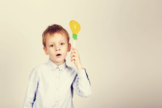 Cute boy with yellow paper lightbulb against a white background. little student holding toy bulb. Cheerful smiling Kid with funny photo props. School concept. Back to School