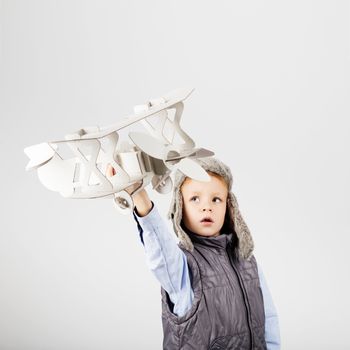 Child boy playing with paper toy airplane and dreaming of becoming a pilot against a white background