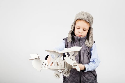 Child boy playing with paper toy airplane and dreaming of becoming a pilot against a white background