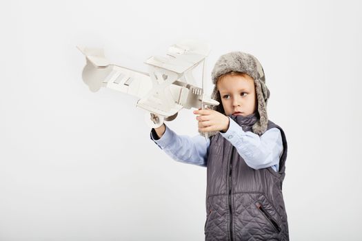 Child boy playing with paper toy airplane and dreaming of becoming a pilot against a white background