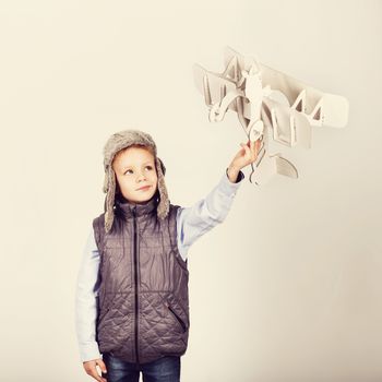 Child boy playing with paper toy airplane and dreaming of becoming a pilot. Retro toning.