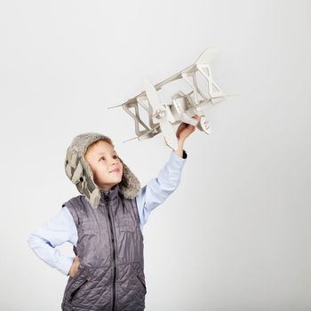 Child boy playing with paper toy airplane and dreaming of becoming a pilot against a white background