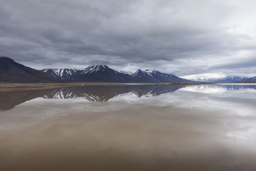 Beautiful scenic view of blue gulf under barren mountain range with melting snow against the background of dramatic evening sky near Barentsburg, Spitsbergen (Svalbard island), Norway, Greenland sea

