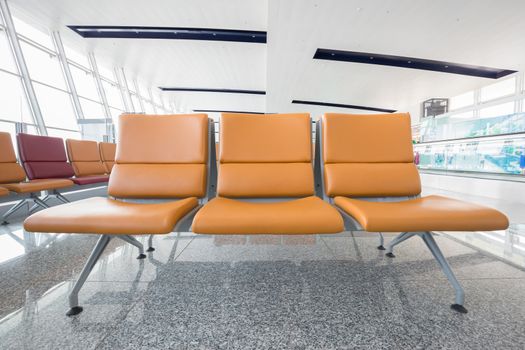Close focus on three leather chairs in orange color which connected together as a bench on shiny marble floor in white building