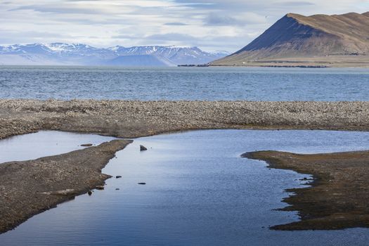 Beautiful scenic view of blue gulf under barren mountain range with melting snow against the background of dramatic evening sky near Barentsburg, Spitsbergen (Svalbard island), Norway, Greenland sea

