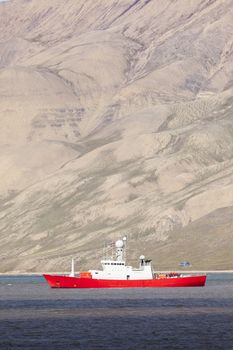 Beautiful scenic view with norge cruise boat docked at Longyearbyen port against the background of fogged black mountain and calm water of Advent Bay, Spitsbergen (Svalbard), Norway, Greenland sea

