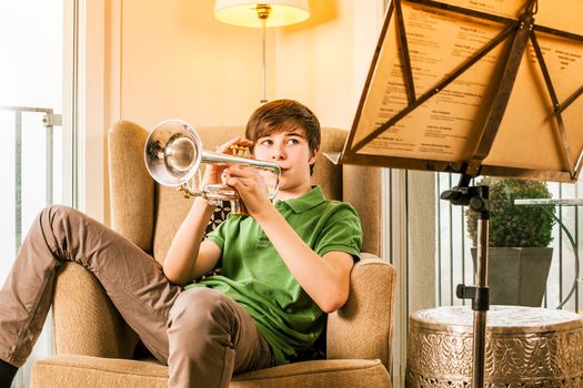 Photo of a teenage male practicing his trumpet at home.