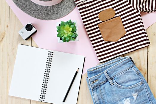 Fashion concept : Lady's outfit with jeans short, blank notebook paper and action camera on wooden background, casual outfit for teenage girls