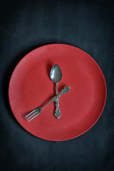 Clock with red plate, spoon and fork  on rusty background