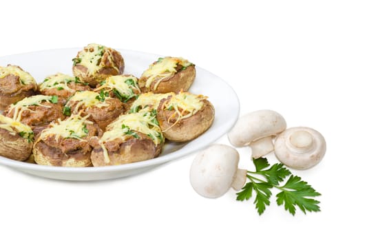 Baked button mushrooms stuffed with minced meat, cheese and greens on the white dish and several uncooked mushrooms with parsley twig beside closeup on a light background
