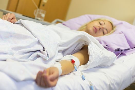 Bedridden female patient lying in hospital bed, receive infusion while recovering after surgery.