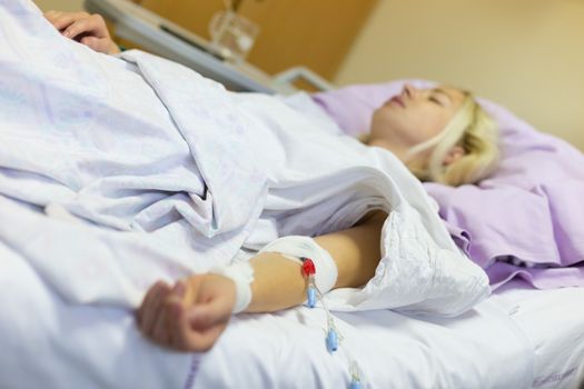 Bedridden female patient lying in hospital bed, receive infusion while recovering after surgery.