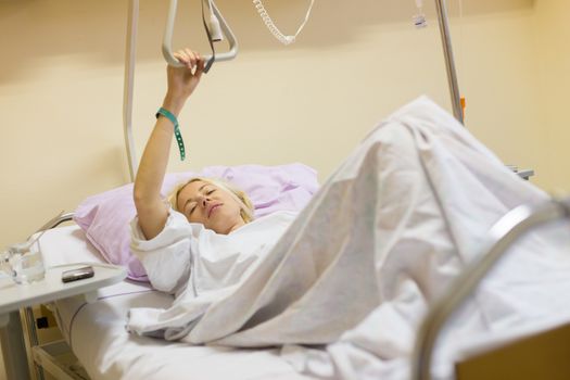 Bedridden female patient lying in hospital bed, recovering after surgery.