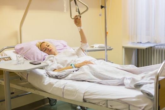 Bedridden female patient lying in hospital bed, recovering after surgery.