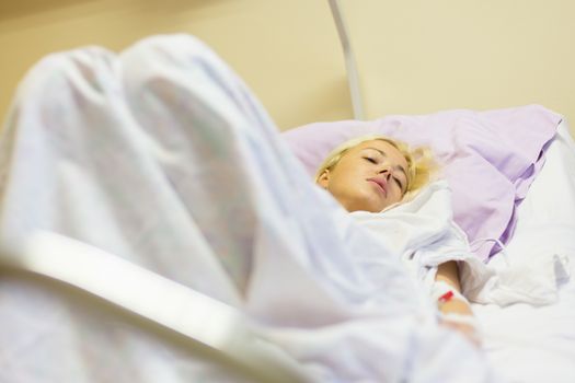 Bedridden female patient lying in hospital bed, recovering after surgery.