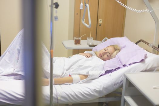 Bedridden female patient lying in hospital bed, recovering after surgery.