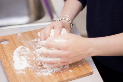 female hands in flour closeup kneading dough on table