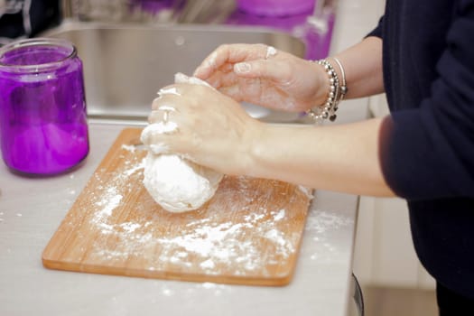 female hands in flour closeup kneading dough on table