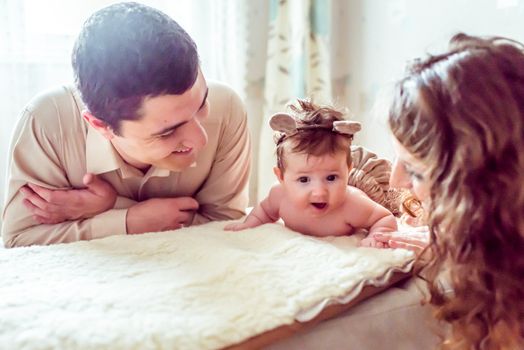 naked baby with her parents lying on soft blanket in the room