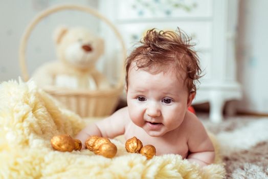 naked baby lying on a yellow soft blanket with decorated golden nuts in the room