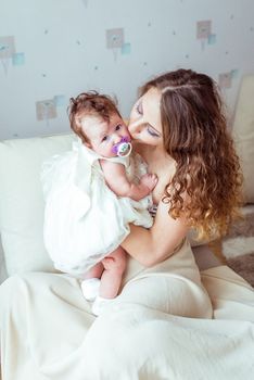 mother holding baby in her arms in a white dress in a room