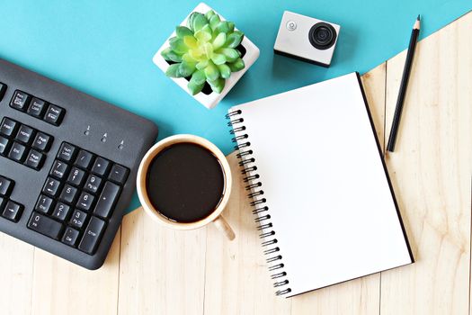 Business concept : Flat lay style of office workspace desk with blank notebook paper, computer keyboard, cup of coffee and action camera, top view mock up