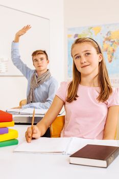 Photo of two teenagers in a classroom happy and lifting their hands to answer a question.