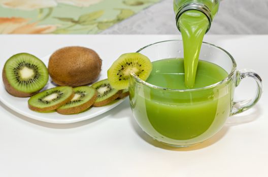 Fresh KIWI juice is poured from a bottle into a Cup, piece of fruit on the Cup and the plate nearby. Selective focus. Place for text.