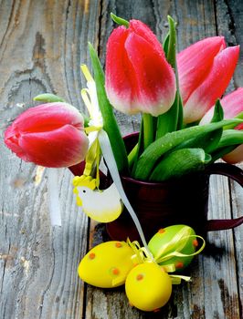 Bunch of Magenta Tulips in Watering Can with Colored Easter Eggs and Handmade Chicken Figure closeup on Rustic Wooden background