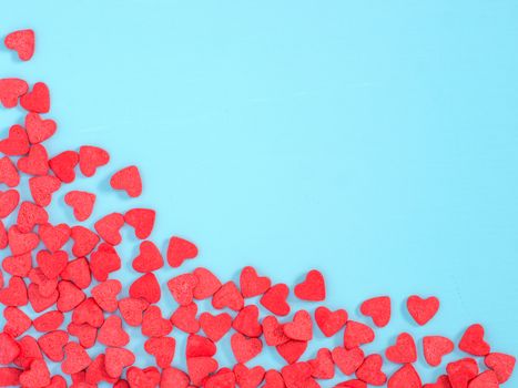 Border frame of red hearth-shape sprinkles on blue background with copyspace. Top view or flat lay