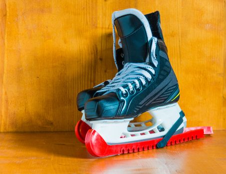 Professional hockey skates with red protective covers, against the wooden background

