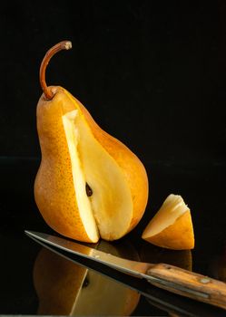 Pear, a knife and a cut  slice  on a black background with reflection