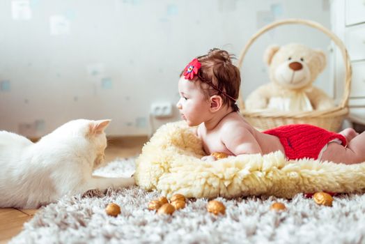 naked baby lying on soft blanket and watching a cat