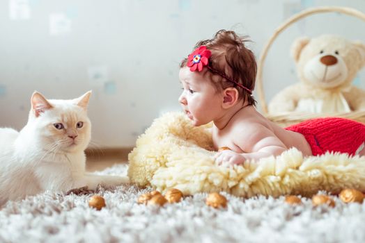 naked baby lying on soft blanket and watching a cat