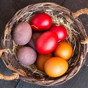 Wicker basket with colorful Easter eggs on wooden table, closeup