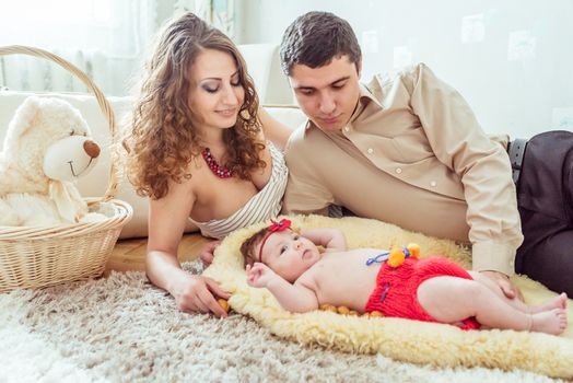 naked baby with her parents lying on soft blanket in the room