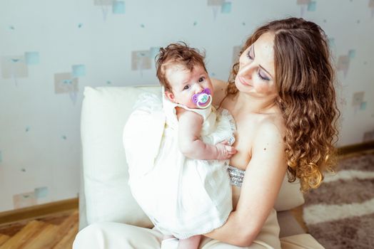 young woman holding baby in her arms in a white dress in a room