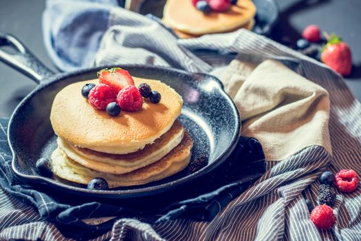 Home made pancakes with berries on metal frying pan decorated with berries (blueberries, raspberries and blackberries). Top View.