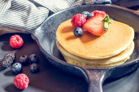 Home made pancakes with berries on metal frying pan decorated with berries (blueberries, raspberries and blackberries). Top View.