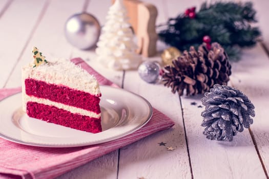 Christmas cake on plate on red fabric on wood background and decorations.