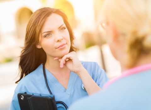 Two Young Adult Professional Female Doctors or Nurses Talking Outside.