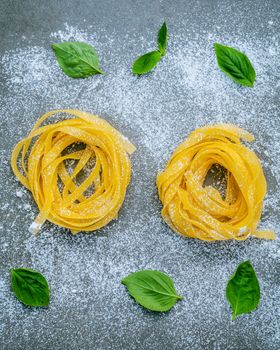 Italian food concept pasta with sweet basil with flour setup on concrete background. Homemade tagliatelle. Raw pasta on the concrete background. Food background top view .